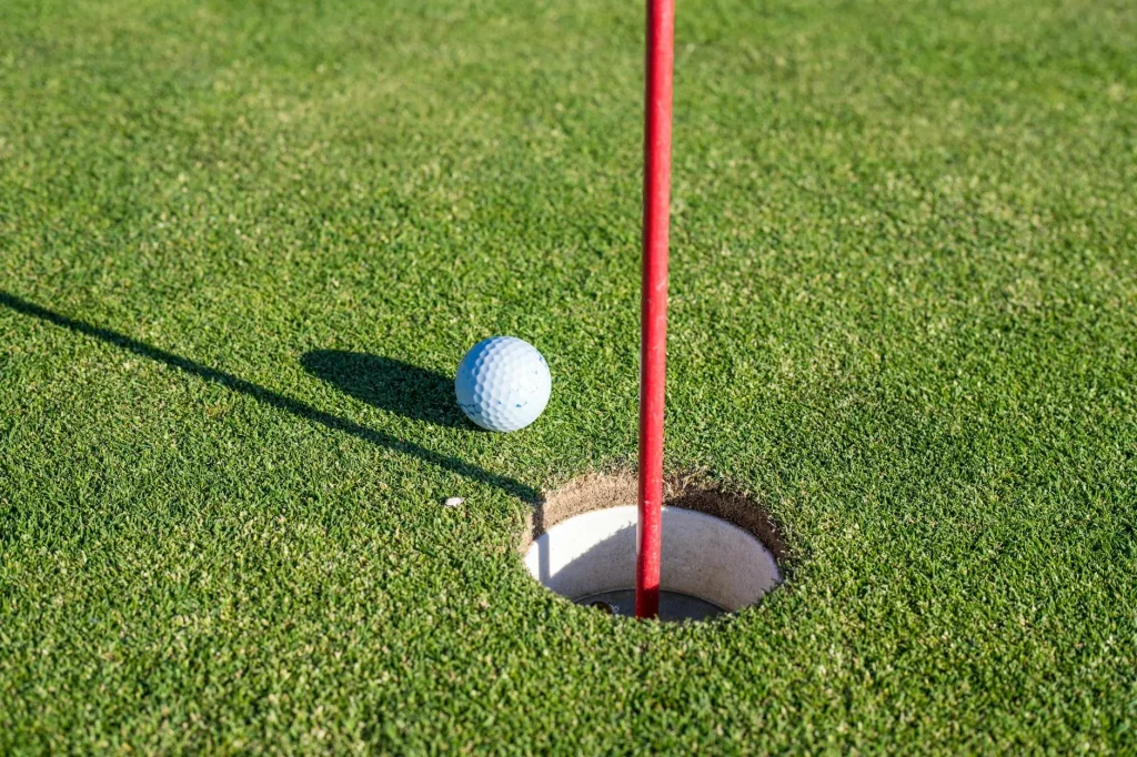 Golf ball near the hole on a putting green in warm sunlight