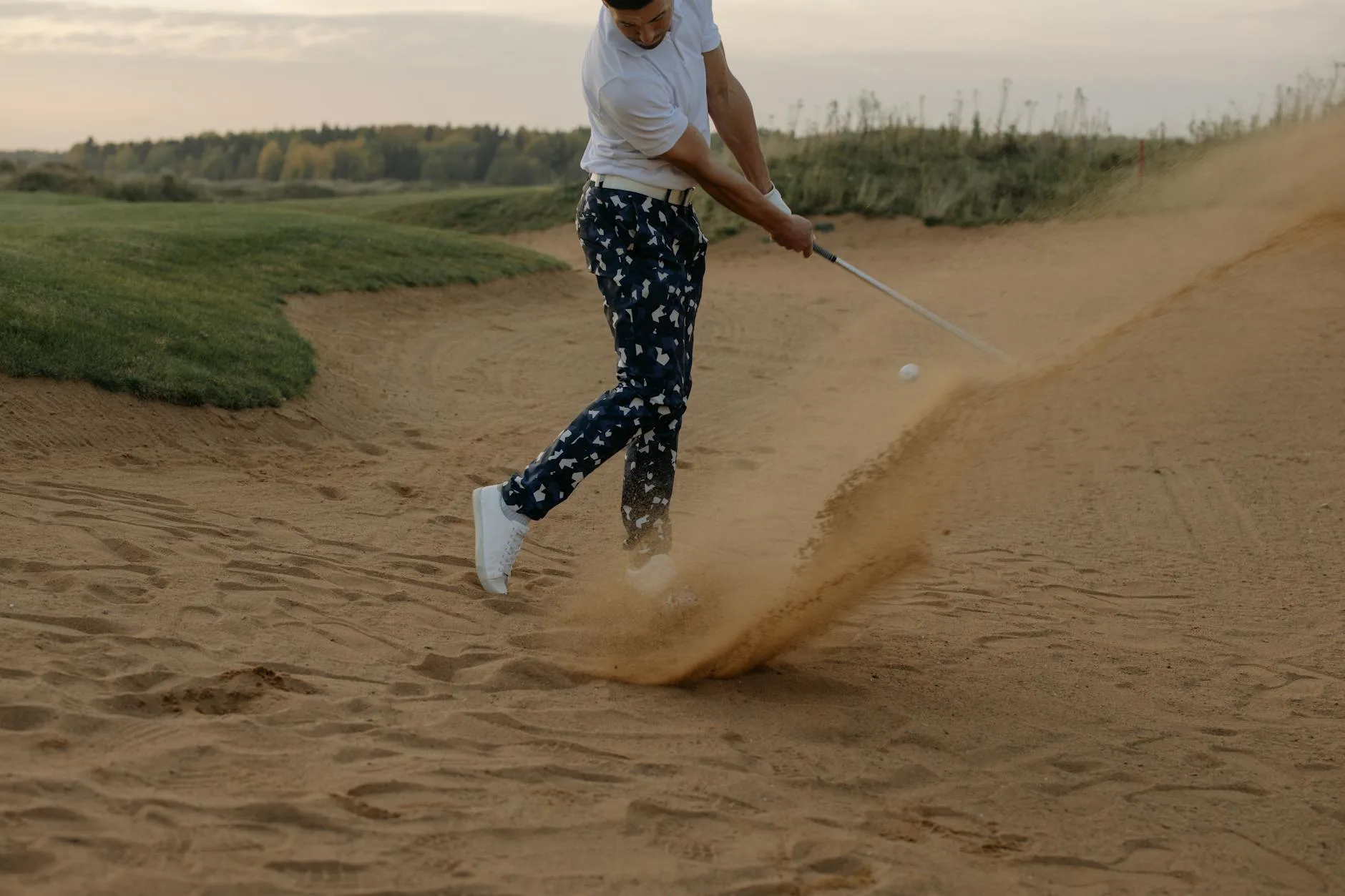 Golfer raking sand bunker after playing a shot