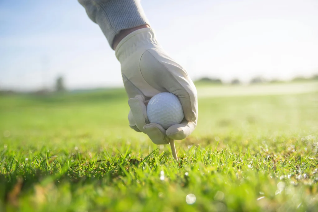 Golfer placing ball on tee close up on green golf course