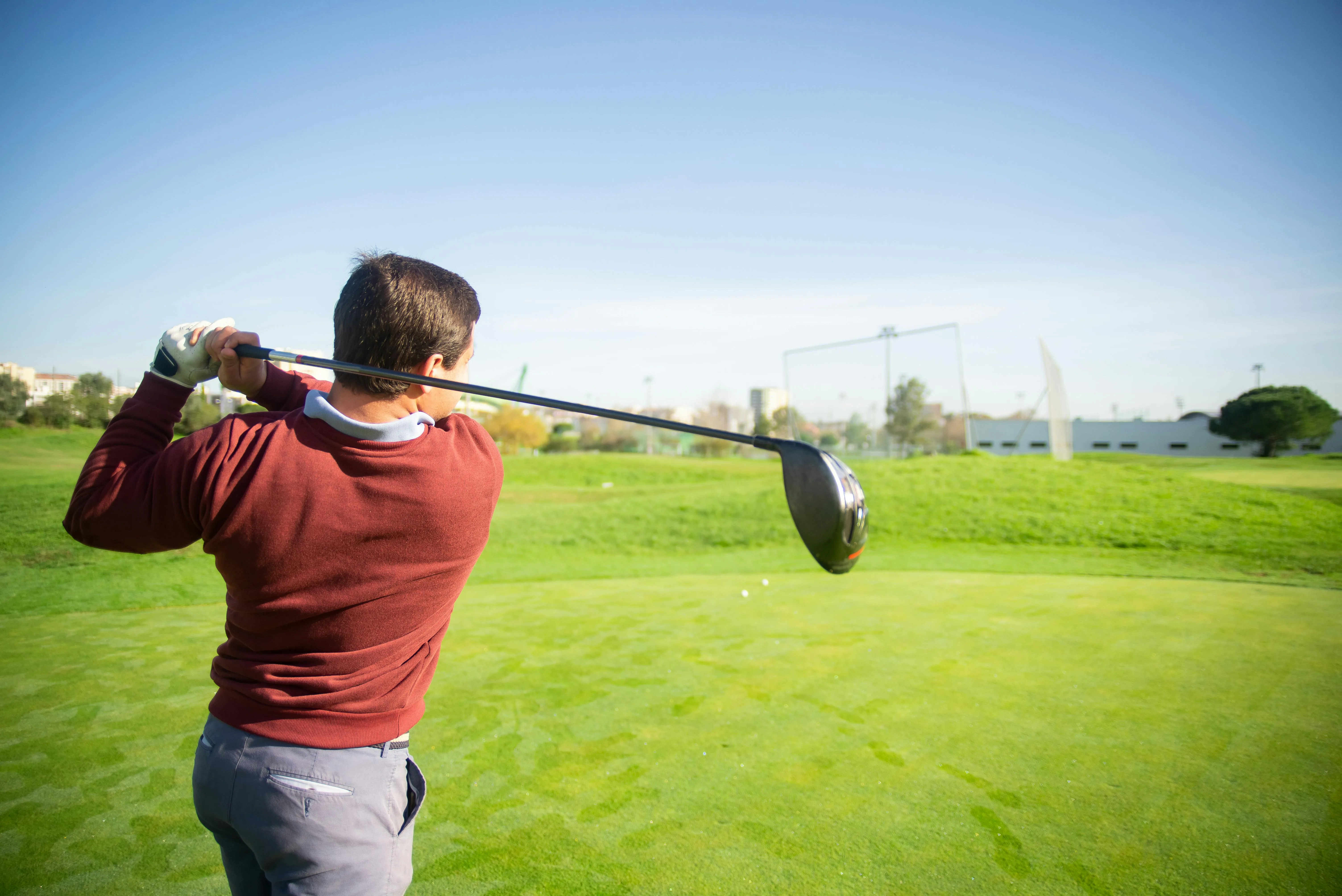 Golfer mid-swing with driver on tee box green course