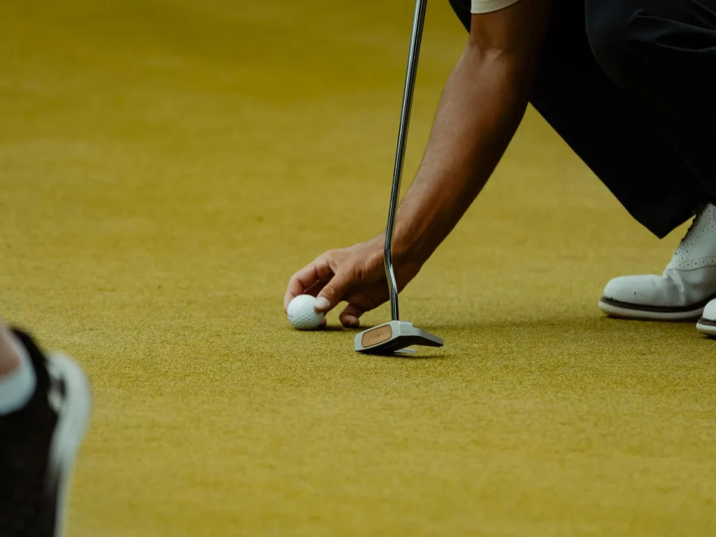 Golf putter head behind a ball on a putting green